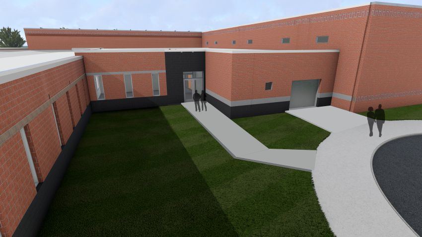 A close-up rendering of the main entrance to the safety connector. A concrete path leads to glass double doors set into a dark gray entrance block. To the right, a rolling garage-style door is visible on the red brick wall, and silhouette figures stand near the entryway.