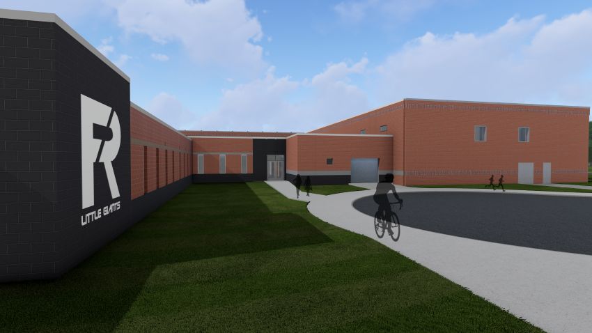 A 3D architectural rendering of the Fremont Ross High School safety connector under a bright blue sky. To the left, a dark gray masonry wall features a large white 'R' logo with the text 'LITTLE GIANTS.' This connects to a red brick building with a curved driveway in the foreground, where silhouette figures are depicted walking and cycling.