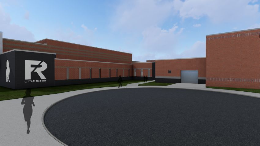 A ground-level perspective of the building exterior. In the foreground, a silhouette of a jogger runs along a sidewalk near the circular driveway. The view highlights the contrast between the dark gray logo wall and the long section of red brick façade with rectangular windows.