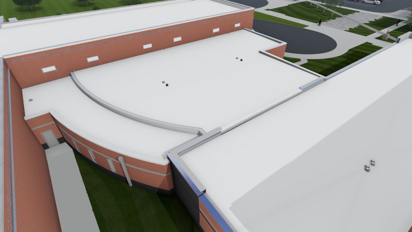 A high-angle aerial view focusing on the rear or side of the facility. It highlights a curved brick wall section and the clean lines of the white roofing membrane. A parking lot and green space are visible in the background.